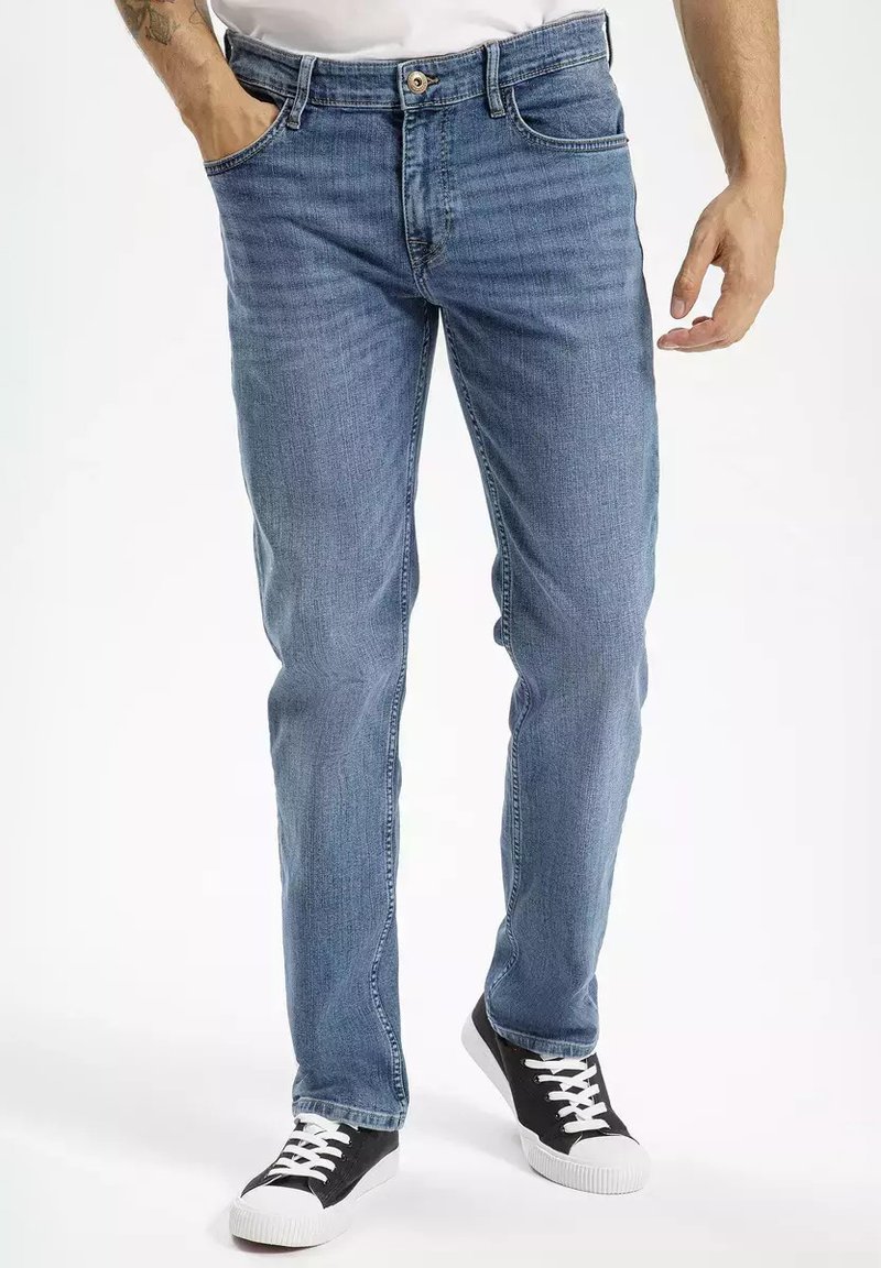 Jasnoniebieskie dżinsy o prostym kroju, pięć kieszeni, żółte szwy i klasyczne zapięcie na guzik, w połączeniu z czarnymi trampkami.