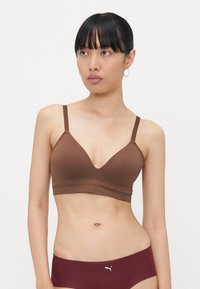Reggiseno wireless marrone con design a V, spalline sottili regolabili e texture liscia. Presenta un piccolo logo bianco sulla fascia.