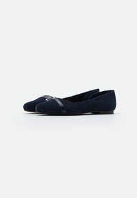 Marineblå mokkasiner i semsket skinn med en blank svart accentbånd over tåen. Rund tådesign, myk tekstur og flat såle for komfort.