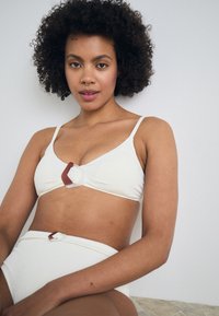 White textured bikini set featuring a triangular bra with a geometric brown plastic accent, matching high-waisted bottoms, on a model.