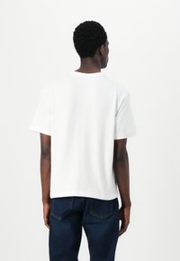 White cotton t-shirt with a relaxed fit, short sleeves, and a round neckline, paired with dark blue denim jeans. Minimalist design.