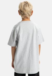 Šedé bavlněné tričko s krátkými rukávy a kulatým výstřihem, zobrazené zezadu. Má volný střih a minimální detaily šití.