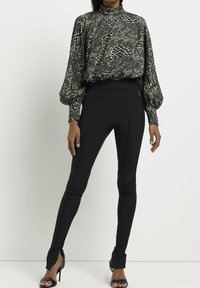 Pantalon noir ajusté associé à un blouse à col haut avec un imprimé animal gris et crème, à manches longues et avec des poignets volumineux.
