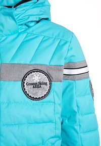 Doudoune turquoise avec des rayures grises et des patchs ronds. Texture lisse avec des coutures matelassées et une capuche. Accentué par des lignes blanches.