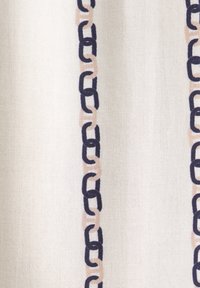 Textil mit einem cremefarbenen Hintergrund und einem sich wiederholenden Kettenmuster in dunklem Blau und hellbeigen Farbtönen, das eine strukturierte Oberfläche aufweist.