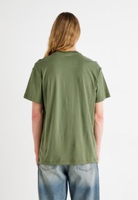 T-shirt in cotone verde oliva con colletto girocollo, maniche corte e vestibilità comoda. Il tessuto presenta una texture liscia e un design informale.