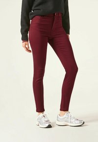 Jeans skinny burdeos hechos de tejido elástico, con una cintura alta y una textura suave. Combinados con zapatillas deportivas plateadas.