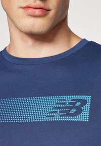 Mörkblå bomullströja med rund halsringning, som har ett strukturerat ljusblått geometriskt mönster och logotyp på framsidan.