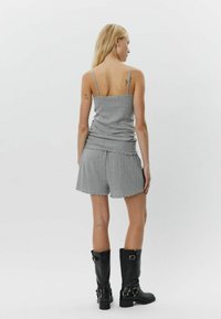 Sivi pleteni top bez rukava s tankim naramenicama, uparen s odgovarajućim šortsevima s izrezanim rubom, i sjajnim crnim čizmama do koljena.