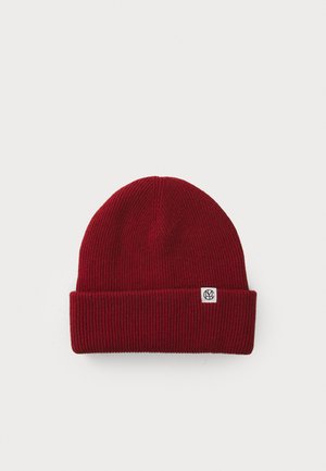 Rød ribbestrikket lue med brett, og liten logo-tag. Har en glatt tekstur og rund topp for en tett passform.