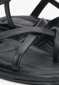 Zwarte leren teenslippers met meerdere dunne banden die zijn verweven over een gestructureerde voetbed, met een zachte, gebogen zool voor comfort.