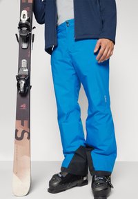 Helle blaue Skihosen mit einem schlanken Design, hergestellt aus wasserdichtem Material. Verfügt über verstellbare Bündchen und verstärkte schwarze Akzente am Saum.