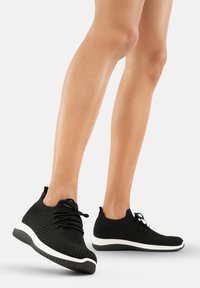 Sneakers neri in maglia con suole bianche, caratterizzati da una tomaia testurizzata, forma arrotondata e chiusura con lacci tradizionale per una vestibilità sicura.