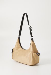 Beige nylon válltáska ívelt formával, fekete állítható pánttal, ezüst színű fémalkatrészekkel és cipzárral zárható. Simább textúrával, minimális részletezéssel.