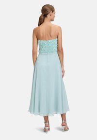 Miętowa sukienka z bezramiennym koronkowym topem w kwiaty i zwiewnym, przezroczystym dołem. Posiada zamek błyskawiczny z tyłu oraz srebrne szpilki.