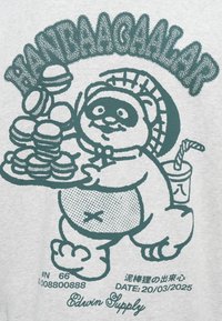Camiseta gris con un gráfico en verde azulado de un panda de dibujos animados sosteniendo una bandeja de macarons, con una bebida y un texto caprichoso arriba.