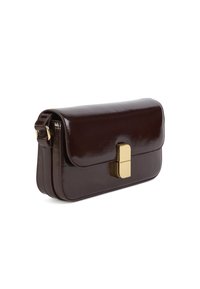 Sac à main en cuir brun foncé brillant avec un fermoir rectangulaire en or et une sangle réglable sur un fond blanc.