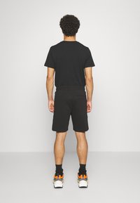 T-shirt noire et shorts noirs, en matériau coton. La vue de dos montre un design ajusté, une texture lisse, et des baskets avec des accents orange.