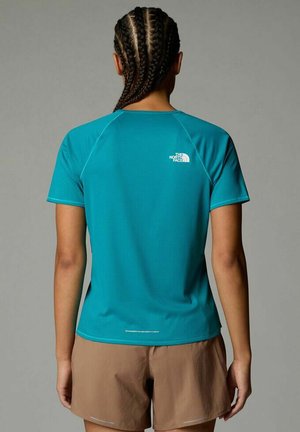 Camiseta deportiva turquesa de manga corta, con tejido texturizado y detalle reflectante en la parte posterior. Combinada con pantalones cortos marrones.