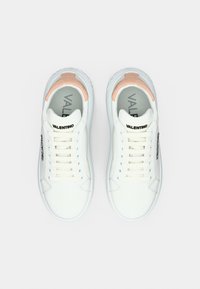 Άσπρα δερμάτινα αθλητικά παπούτσια με απαλό ροζ λεπτομέρεια στη φτέρνα. Η γλώσσα φέρει το λογότυπο της μάρκας· οι κορδόνια είναι γαλάζια. Η σόλα έχει χαμηλό προφίλ σχεδιασμό.