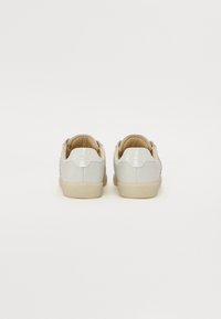 Sneakers bianchi in pelle verniciata con una superficie liscia, fodera beige e suola piatta. Presentano un design del tacco discreto e una branding minimale.