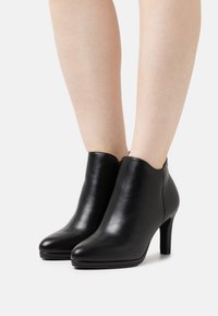 Botines negros de cuero con textura suave, punta puntiaguda y un tacón de aguja moderado. Diseñados con un corte bajo alrededor del tobillo.