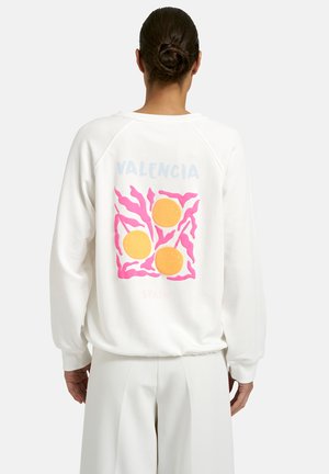 Person with hair in bun wearing white sweatshirt with pink abstract shapes and three orange circles, text "Valencia" on back.