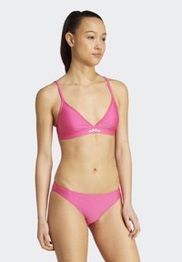 Růžový plavkový set s trojúhelníkovým braletem a odpovídajícími vykrojenými spodními částmi. Tkanina vypadá hladce a na vršku se nachází logo Adidas.