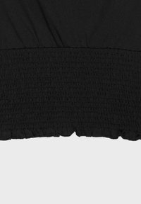 Gros plan d'un tissu noir avec couture smockée élastique et ourlet froncé à volants en bas.