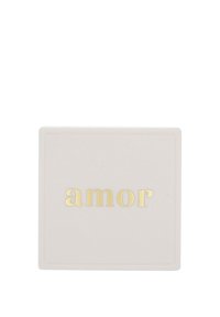 Vitt kvadratiskt med guldemboserat ord "amor" centrerat på ytan, minimalistisk design.