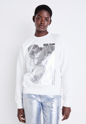 White sweatshirt with metallic silver graphic and "REAL ICON" text. Paired with shiny silver pants. Smooth texture, crew neck design.