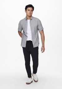 Camisa de botones de manga corta en gris sobre una camiseta blanca, combinada con pantalones ajustados negros y zapatillas blancas con detalles en gris.