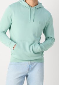 Mátově zelená mikina s kapucí vyrobená z měkké bavlněné směsi, má klokaní kapsu, nastavitelnou kapuci se stahovací šňůrkou a malé logo na hrudi.