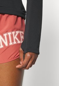 L ähikuva henkilön kädestä, joka lepäilee reidellä, pukeutuneena punaisiin Nike-shorteihin ja pitkään mustaan hihaan, jossa on peukalonreikä.