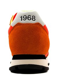 Zapatilla de estilo retro con un tacón trasero de ante naranja, una caperuza blanca en el talón con "1968" y suela de goma negra; acentos de diseño vibrantes.