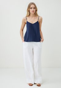 Marine satijnen top met dunne bandjes, gecombineerd met losse, witte linnen broeken. De outfit heeft een relaxte pasvorm en gladde texturen.