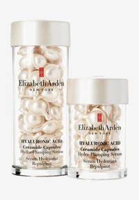 Klart glasbehållare fyllda med glänsande, vita keramikkapslar, täckta med silverlock. Etiketter visar produktnamn och märke.