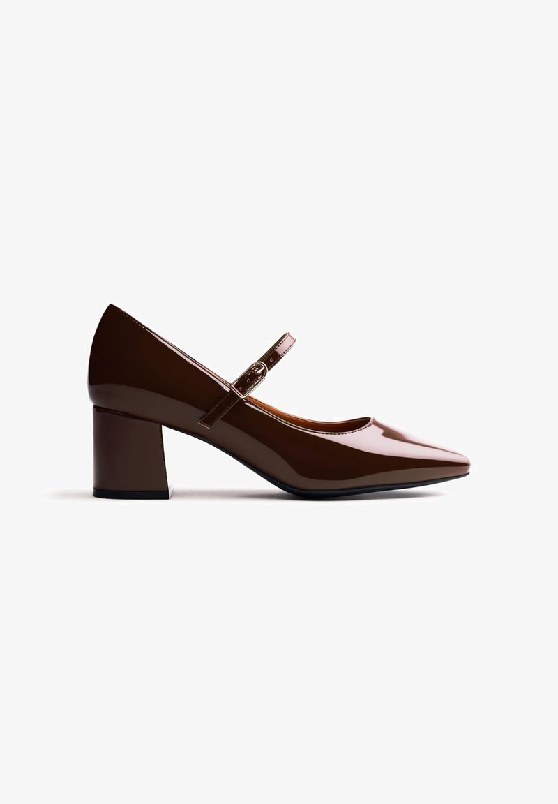 Chaussure Mary Jane en cuir verni marron avec petit talon carré et bride réglable sur fond blanc.