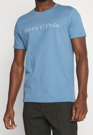 T-shirt di cotone azzurro chiaro con maniche corte, dotato di un colletto tondo e con il testo "Marc O'Polo" stampato in bianco sul petto.