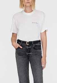 Hvid bomulds T-shirt med korte ærmer, der har en sort teksttryk på venstre bryst. Sammen med høj talje sorte denim jeans.