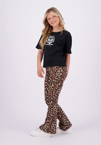 Svart kortermet t-skjorte med hvitt grafisk design, sammen med brune leopardmønstrede vide bukser. Hvite sneakers fullfører antrekket.
