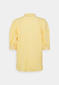 Chemise à manches longues à carreaux jaunes et blancs vue de dos, avec une coupe ample et des poignets froncés.