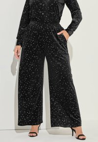 Svarta sammetsbyxor med vida ben som har ett stjärnmönster, elastisk midja, sidofickor och en mjuk textur. Matchas med svarta klackskor.