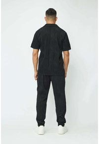 Chemise noire à manches courtes et pantalon assorti à texture ondulée, avec une coupe décontractée et des chaussures blanches. Design épuré et minimaliste.