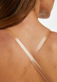 Transparente Riemen, die sich über nackte Haut kreuzen, zeigen eine glatte Textur und subtile Töne und heben ein minimalistisches Design hervor.