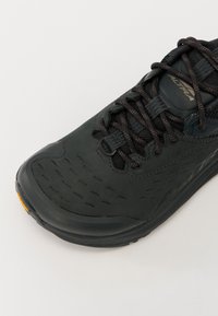 Czarne buty sportowe z fakturowaną cholewką, okrągłym noskiem i czarnymi sznurówkami. Charakteryzują się lekką konstrukcją oraz kontrastującym pomarańczowym akcentem na podeszwie.
