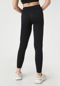 Svarta leggings med hög midja, med strukturerade detaljer och en figurnära passform, kombinerat med ljusfärgade träningsskor.