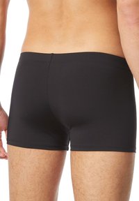 Schwarze Bade shorts aus dehnbarem Material, mit einer enganliegenden Passform, nahtlosen Kanten und einem mittelhohen Bund. Geeignet für Schwimmaktivitäten.