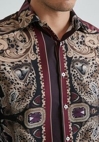 Chemise à boutons à motifs, comportant un mélange de teintes crème, bordeaux foncé et noir, avec des motifs animaliers et des accents ressemblant à des bijoux sur le tissu.