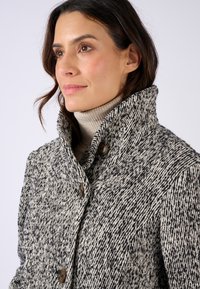 Manteau en mélange de laine avec un motif texturé noir et blanc, doté d'un col haut et de fermetures à boutons marron.